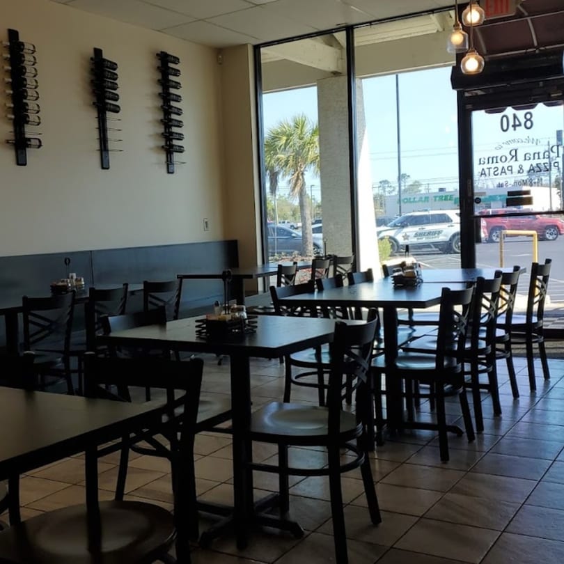 Interior of Pana Roma Pizza & Pasta, with empty tables, chairs, and wine racks on the wall.