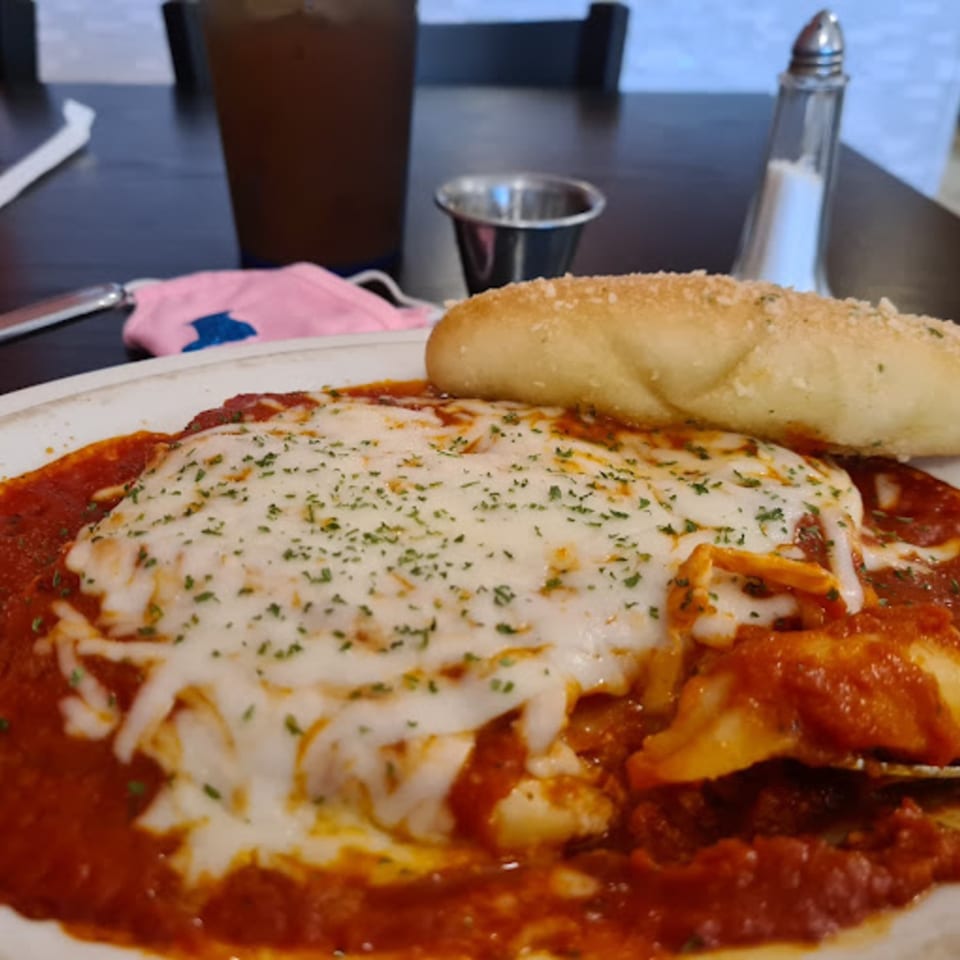 Baked pasta dish with melted cheese and red sauce, served with a breadstick at Pana Roma.