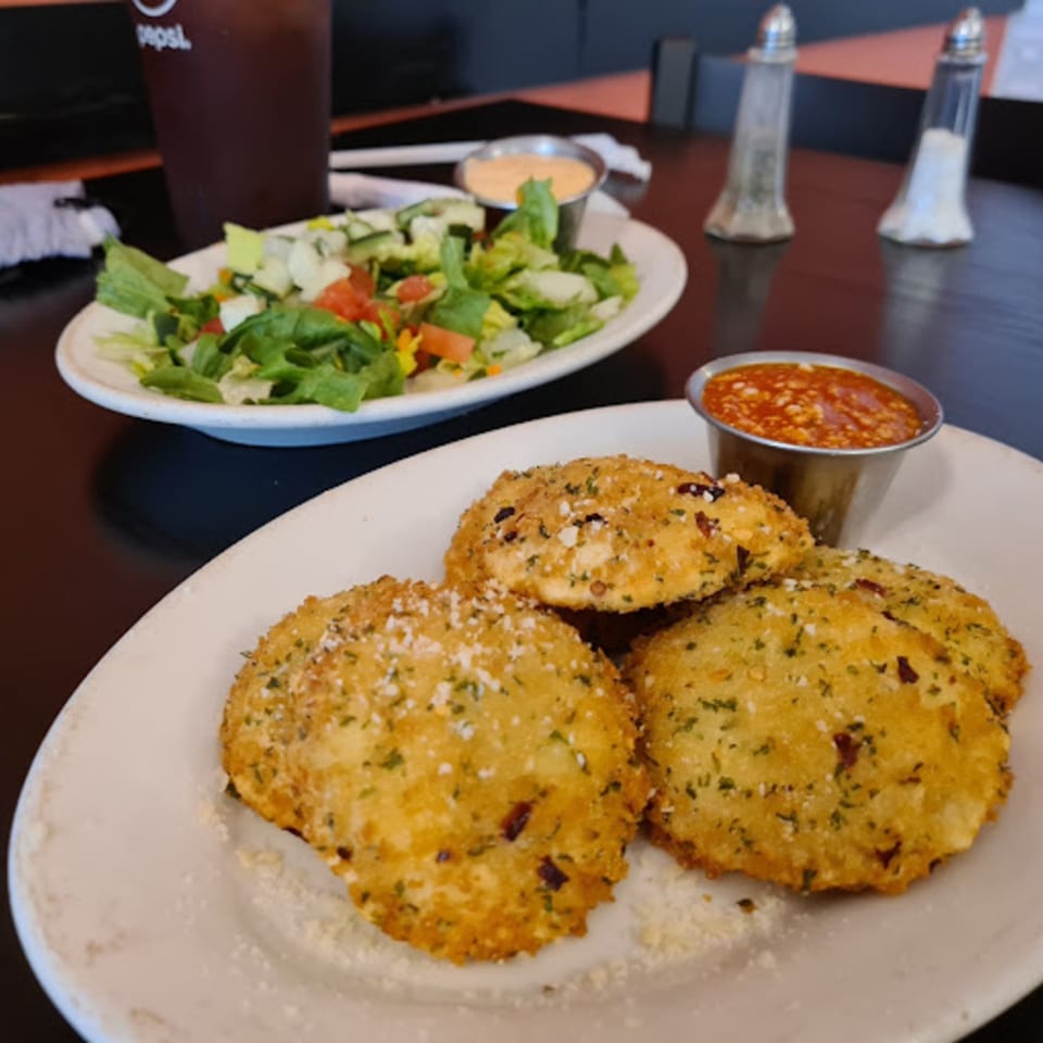 Fried ravioli with marinara sauce, a side salad, and a drink on a dark table.