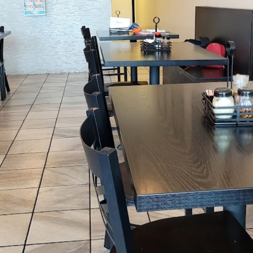 Empty dining area with dark tables and chairs, and light-colored tiled floors.
