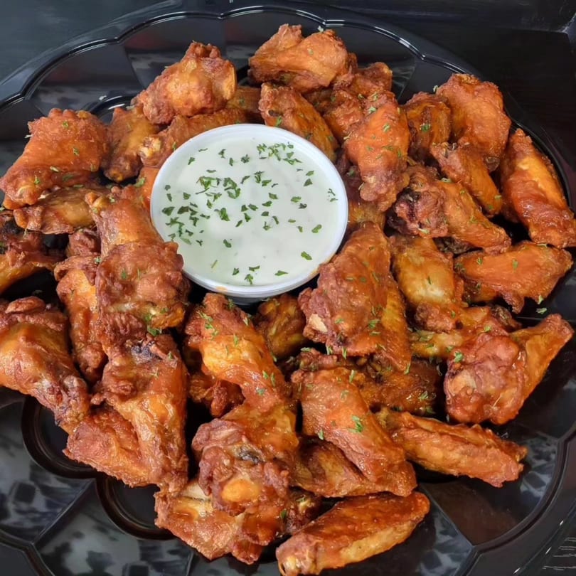 A platter of crispy chicken wings with a side of ranch dressing, garnished with parsley.